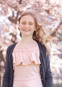 a young girl in a pink dress standing in front of cherry blossoms