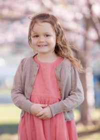 a little girl in a pink dress standing in front of a cherry tree